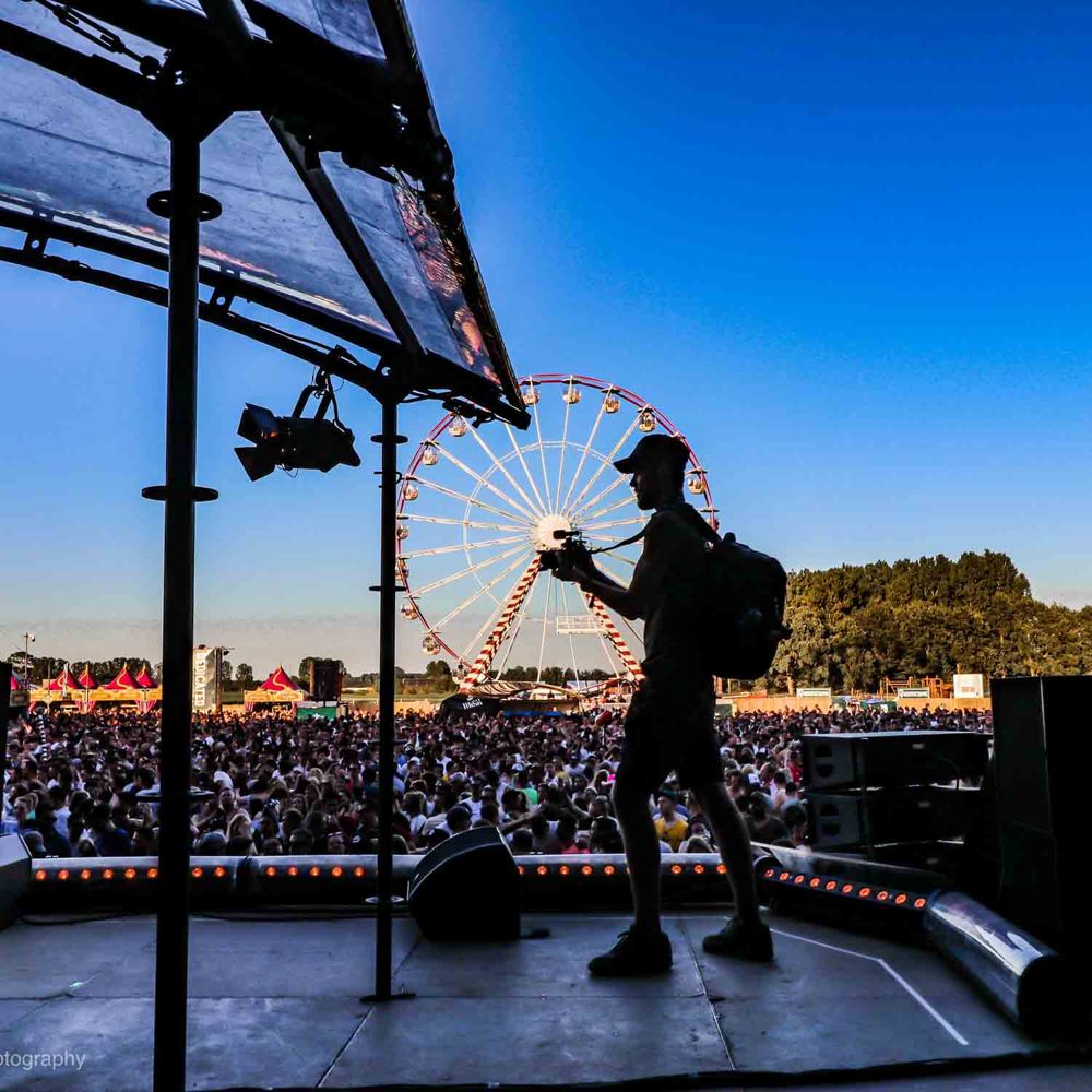 Silhouet van Niek met camera op een podium, met een reuzenrad op de achtergrond